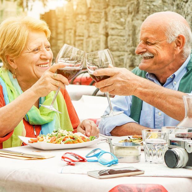 Dos personas tomando una copa de vino mientras comen. Fuente: Bigstock